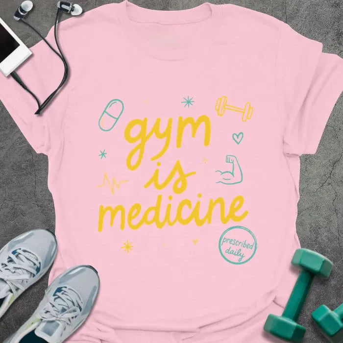 Light pink t-shirt printed with "gym is medicine" in yellow, cyan, and orange, with dumbbell, heartbeat, and smiley graphics