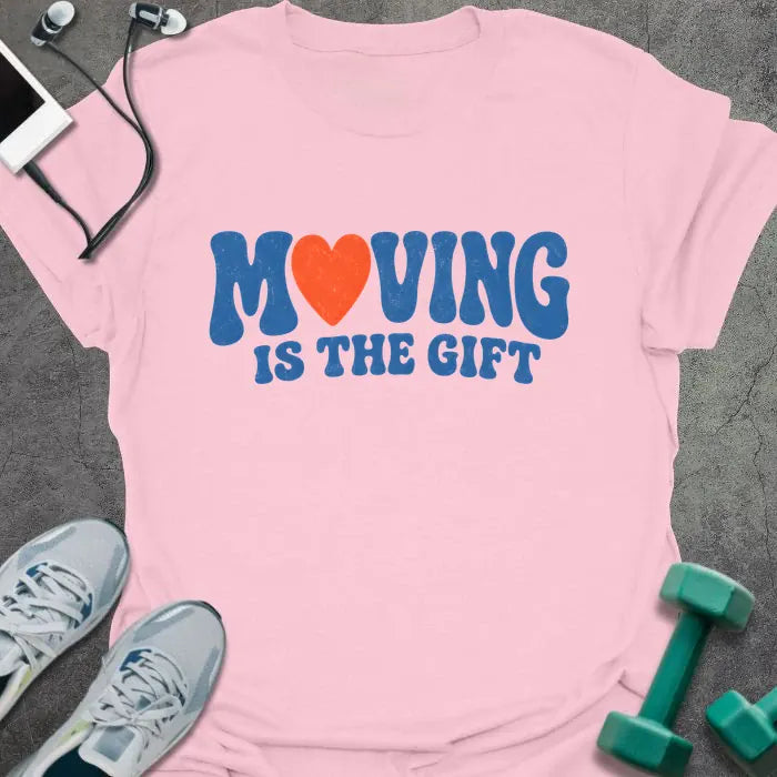 Light Pink t-shirt printed with "MOVING IS THE GIFT" in blue and orange text with a heart replacing the O