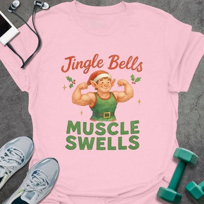 Light pink t-shirt printed with "Jingle Bells MUSCLE SWELLS" in red and green, with an illustration of a leprechaun flexing