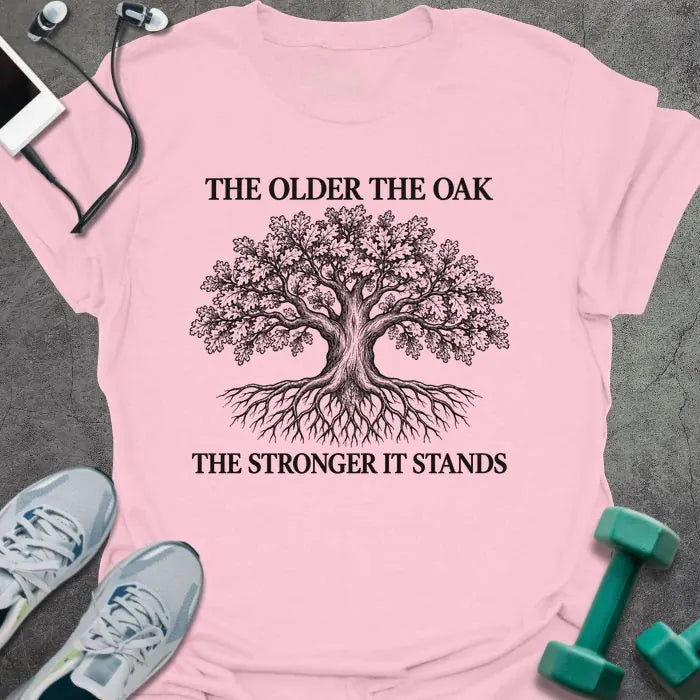 Light pink t-shirt printed with "THE OLDER THE OAK, THE STRONGER IT STANDS" in black, with a drawing of an oak tree and its roots