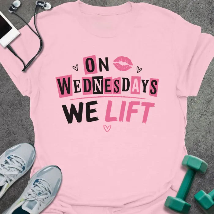 Light pink t-shirt printed with "On Wednesdays We Lift" in pink and black, with an illustration of lips and hearts