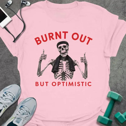 Light Pink t-shirt printed with "BURNT OUT but OPTIMISTIC" in red and black, with skeleton with dumbbells