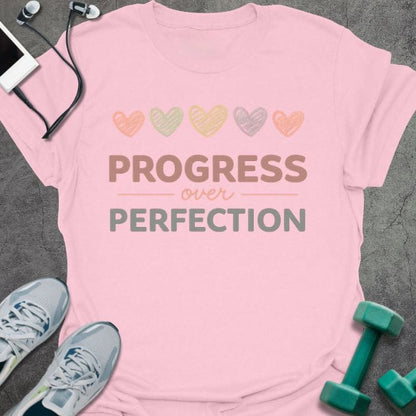 Light pink t-shirt printed with "PROGRESS over PERFECTION" in multi-color, with five hearts in pastel colors