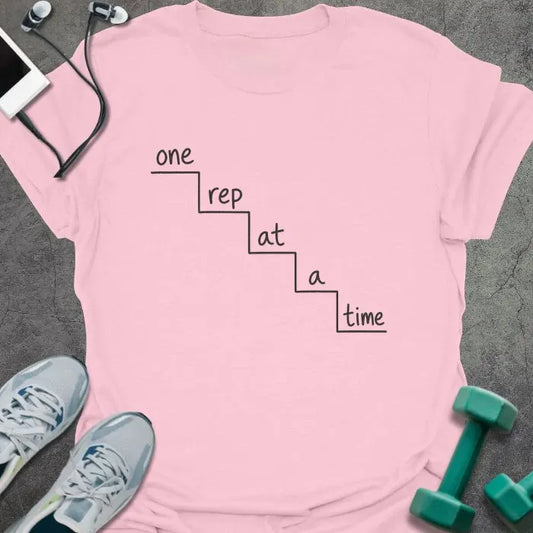 Light pink t-shirt printed with "one rep at a time" in black line art, with staircase graphic