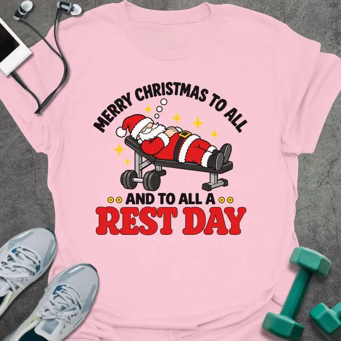Light pink t-shirt printed with "MERRY CHRISTMAS TO ALL AND TO ALL A REST DAY" in black and red, with Santa asleep on a weight bench