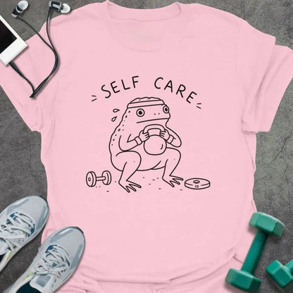 Light Pink t-shirt printed with "= SELF CARE =" in black, with figure exercising with kettlebell and dumbbells