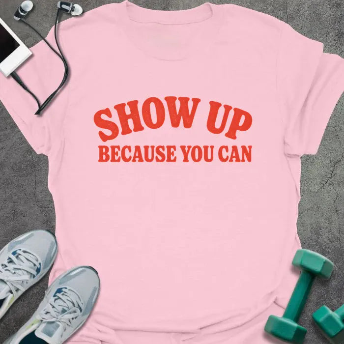 Light Pink t-shirt printed with "SHOW UP BECAUSE YOU CAN" in red bold text