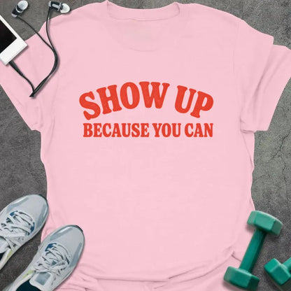 Light Pink t-shirt printed with "SHOW UP BECAUSE YOU CAN" in red bold text