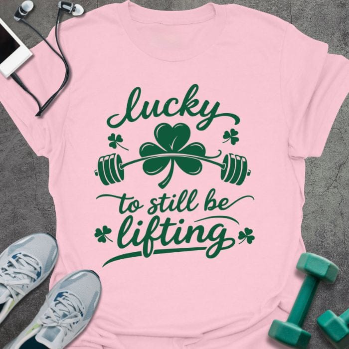 Light pink t-shirt printed with "lucky to still be lifting" in green, with clover, shamrock and barbell