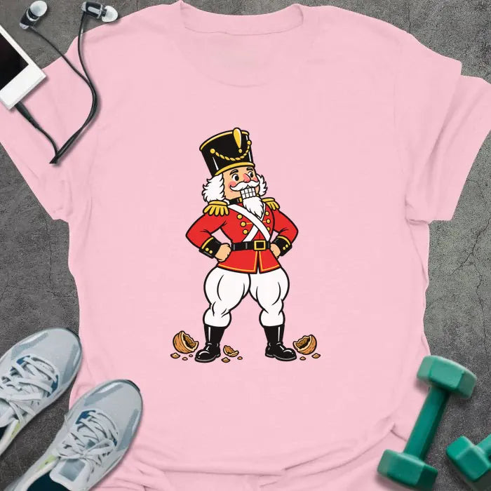 Light pink t-shirt printed with a vintage nutcracker soldier with strong legs, hands on hips, standing over cracked nutshells