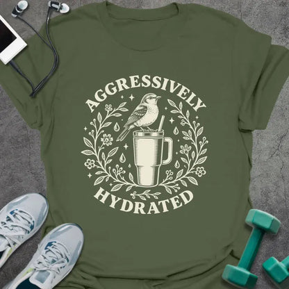Military green t-shirt printed with "AGGRESSIVELY HYDRATED" in cream, with a bird perched on a big insulated tumbler inside a wreath of leaves, flowers and water drops