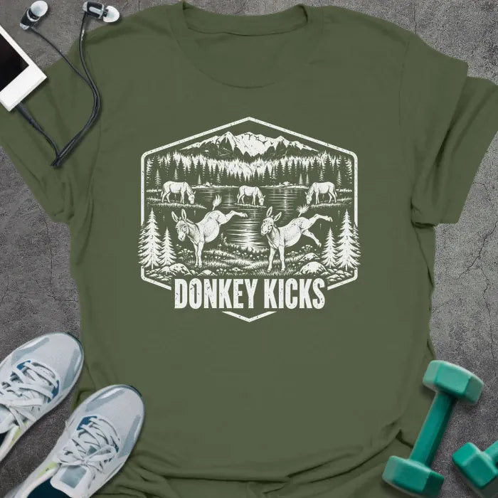 Military green t-shirt printed with "DONKEY KICKS" in white, with two donkeys kicking up their back legs by a mountain lake and pine trees