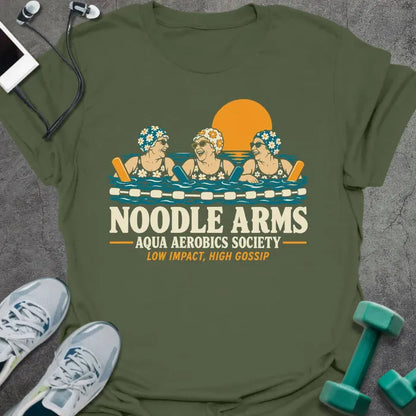 Military green t-shirt printed with "NOODLE ARMS, AQUA AEROBICS SOCIETY, LOW IMPACT, HIGH GOSSIP" in cream and orange, with three older women in flowered swim caps and sunglasses laughing in a pool with pool noodles at sunset