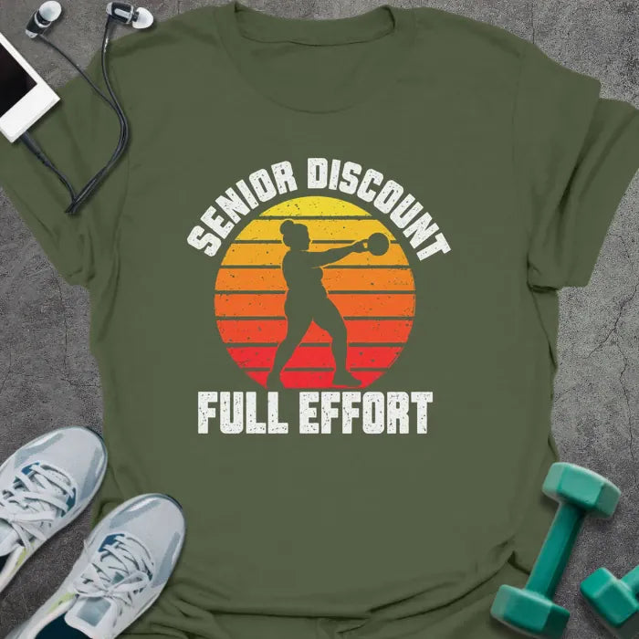 Military green t-shirt printed with "SENIOR DISCOUNT, FULL EFFORT" in white, with a woman swinging a kettlebell against a retro yellow, orange and red sunset