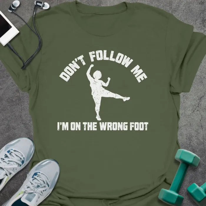Military green t-shirt printed with "DON'T FOLLOW ME, I'M ON THE WRONG FOOT" in white, with an older woman doing an aerobics kick