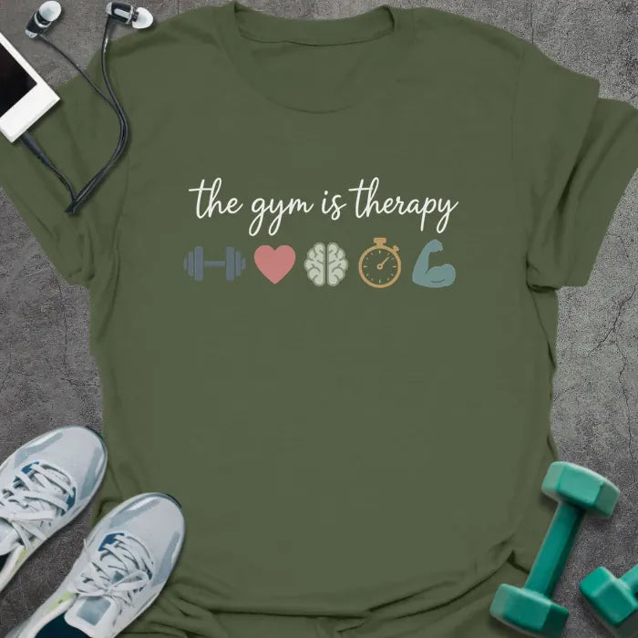 Military green t-shirt printed with "the gym is therapy" in gray, pink, gray, gold, and green, with a dumbbell, heart, brain, stopwatch, and bicep emoji