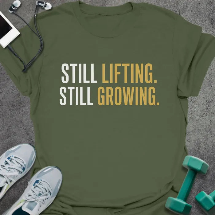 Military green t-shirt printed with "Still Lifting. Still Growing." in white and gold