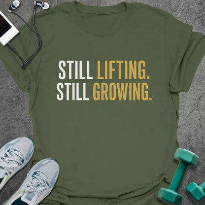 Military green t-shirt printed with "Still Lifting. Still Growing." in white and gold