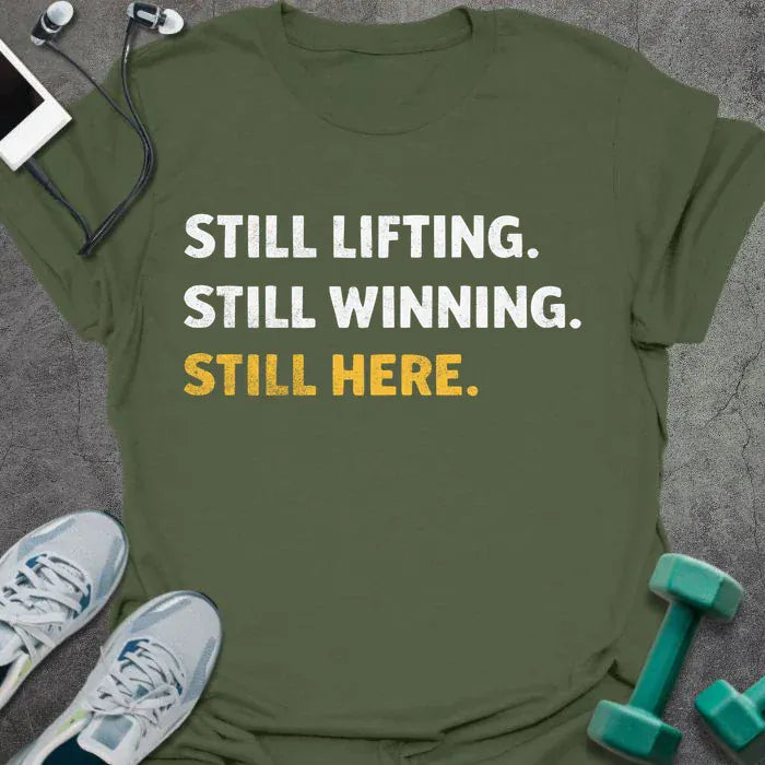 Military green t-shirt printed with "Still Lifting. Still Winning. Still Here." in white and yellow