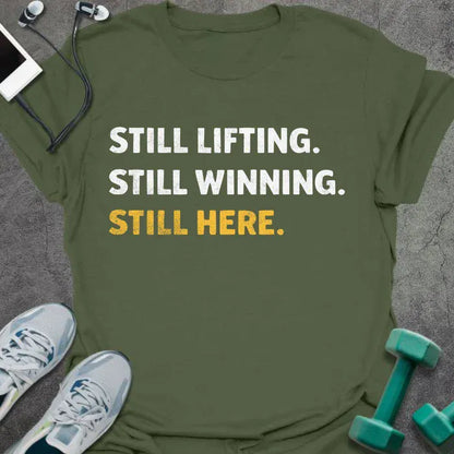 Military green t-shirt printed with "Still Lifting. Still Winning. Still Here." in white and yellow
