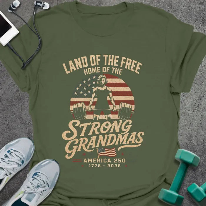 Military green t-shirt printed with "Land of the Free Home of the Strong Grandmas America 250 1776 - 2026" in tan and white, with a weightlifting woman silhouette and American flag