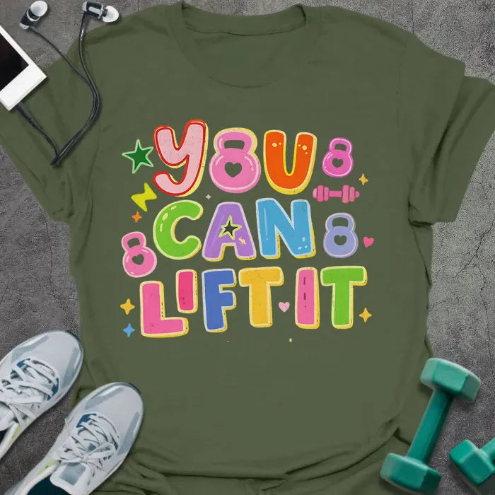 Military green t-shirt printed with "You Can Lift it" in pink, orange, green, purple, blue, yellow, with bubble letters, stars, sparkles, and small dumbbell doodles