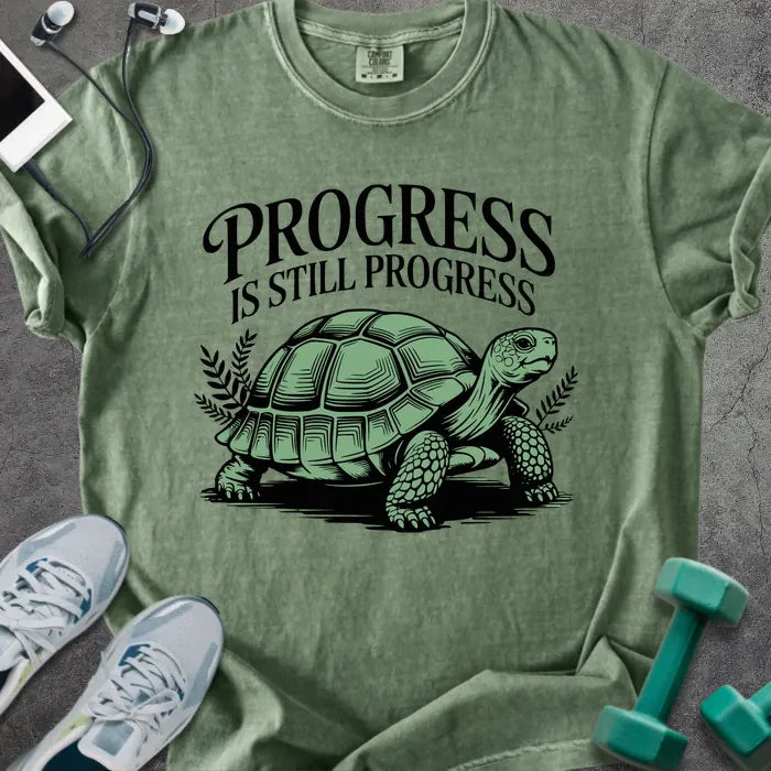 Moss t-shirt printed with "Progress is Still Progress" in green, with a turtle illustration and decorative leaves