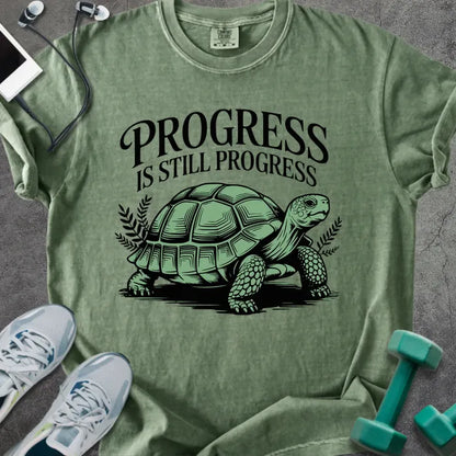 Moss t-shirt printed with "Progress is Still Progress" in green, with a turtle illustration and decorative leaves