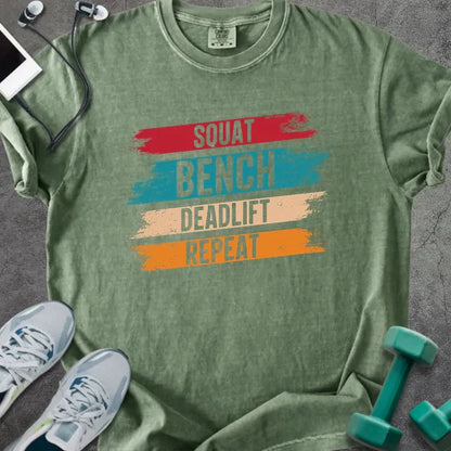 Moss t-shirt printed with "Squat Bench Deadlift Repeat" in red, teal, tan, orange, with red, teal, tan, and orange paint-stroke bands behind the words