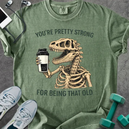 Moss t-shirt printed with "You're Pretty Strong for Being That Old" in green, with skeleton holding a coffee cup