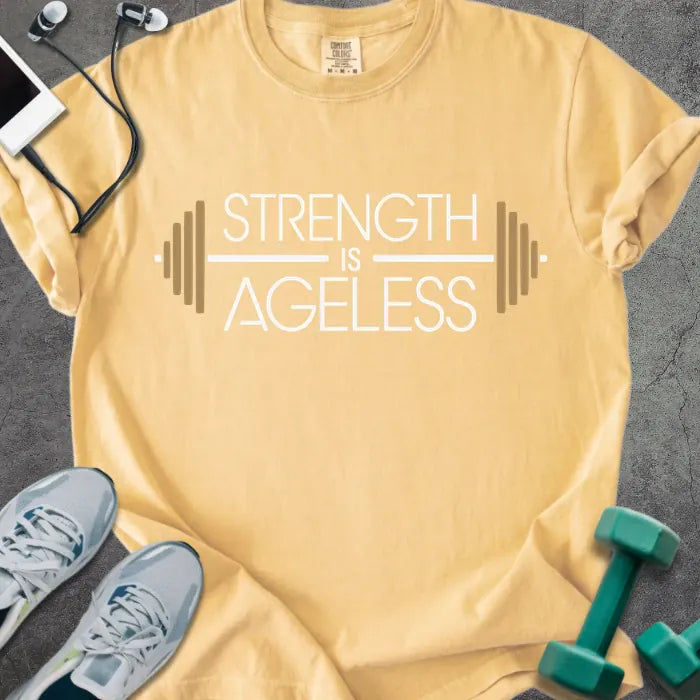 Mustard t-shirt printed with "Strength is Ageless" in white and gold, with a barbell graphic