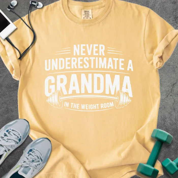 Mustard t-shirt printed with "Never Underestimate a Grandma in the Weight Room" in white, with a barbell graphic