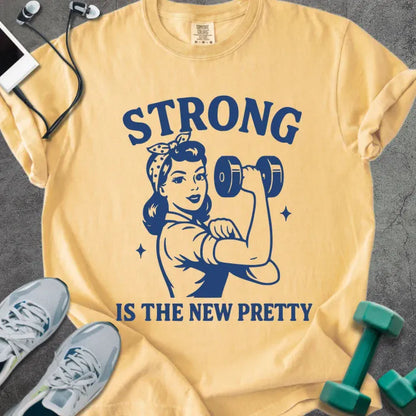 Mustard t-shirt printed with "Strong is the New Pretty" in blue, with a Rosie the Riveter figure with a dumbbell