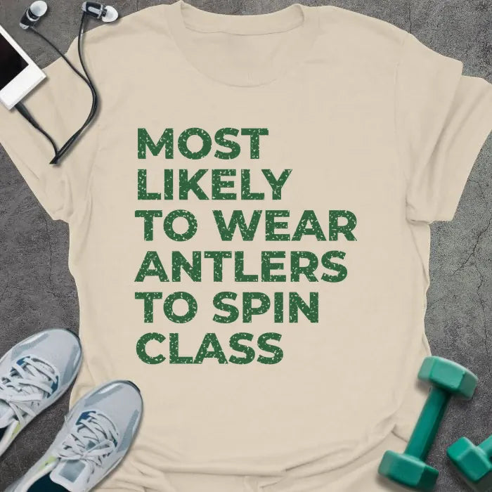 Natural t-shirt printed with "MOST LIKELY TO WEAR ANTLERS TO SPIN CLASS" in green