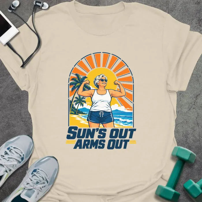 Natural t-shirt printed with "SUN'S OUT ARMS OUT" in navy blue, with a retro beach sunset and an older woman flexing her arms