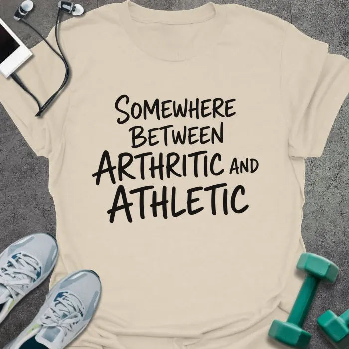 Natural t-shirt printed with "SOMEWHERE BETWEEN ARTHRITIC AND ATHLETIC" in black