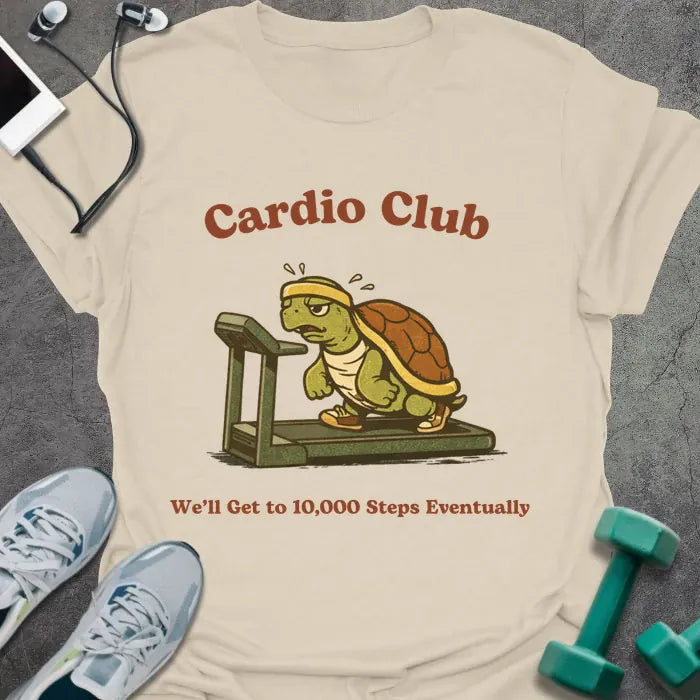 Cream t-shirt printed with "Cardio Club We'll Get to 10,000 Steps Eventually" in brown and red, with turtle on treadmill graphic