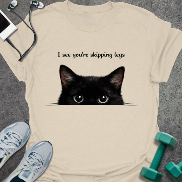 Cream t-shirt printed with "I see you're skipping legs", with a black cat peeking over the bottom edge of the text