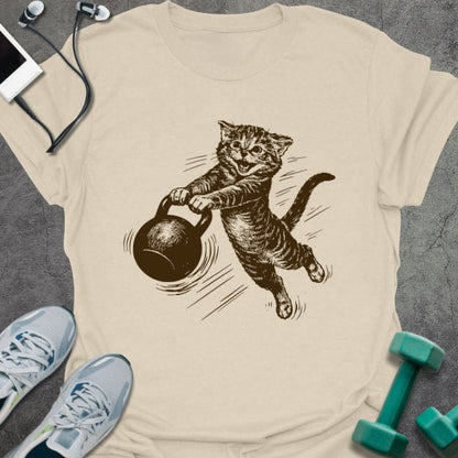 Cream t-shirt with a cat swinging a kettlebell in brown, tan