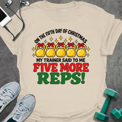 Natural t-shirt printed with "ON THE FIFTH DAY OF CHRISTMAS MY TRAINER SAID TO ME, FIVE MORE REPS!" in black, red and green, with five gold kettlebells tied with red bows