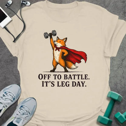 Natural t-shirt printed with "OFF TO BATTLE. IT'S LEG DAY." in black lettering, with a red fox wearing a red cape and holding a dumbbell