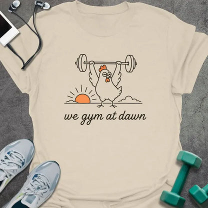 Cream t-shirt printed with "we gym at dawn" in orange, with a bird lifting weights at sunrise