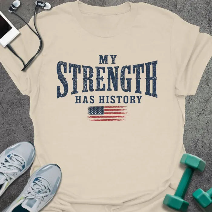 Cream t-shirt printed with "My Strength Has History" in blue and red, with a distressed American flag