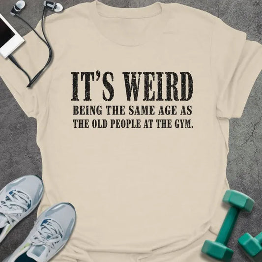Natural T-shirt printed with "IT'S WEIRD BEING THE SAME AGE AS THE OLD PEOPLE AT THE GYM." in brown