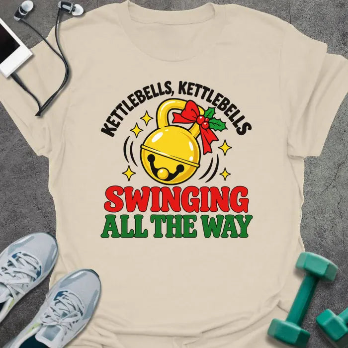 Natural t-shirt printed with "KETTLEBELLS, KETTLEBELLS, SWINGING ALL THE WAY" in black, red and green, with a gold jingle bell kettlebell and holly