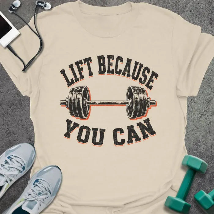 Natural t-shirt printed with "LIFT BECAUSE YOU CAN" in black and red text with a barbell graphic