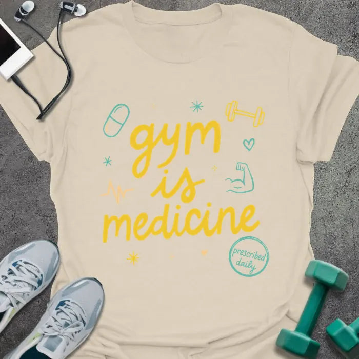 Cream t-shirt printed with "gym is medicine" in yellow, cyan, and orange, with dumbbell, heartbeat, and smiley graphics