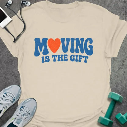 Natural t-shirt printed with "MOVING IS THE GIFT" in blue and orange text with a heart replacing the O