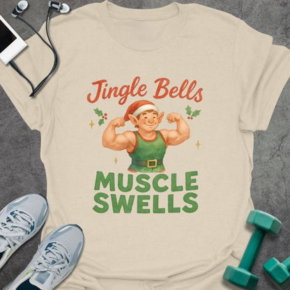 Cream t-shirt printed with "Jingle Bells MUSCLE SWELLS" in red and green, with an illustration of a leprechaun flexing