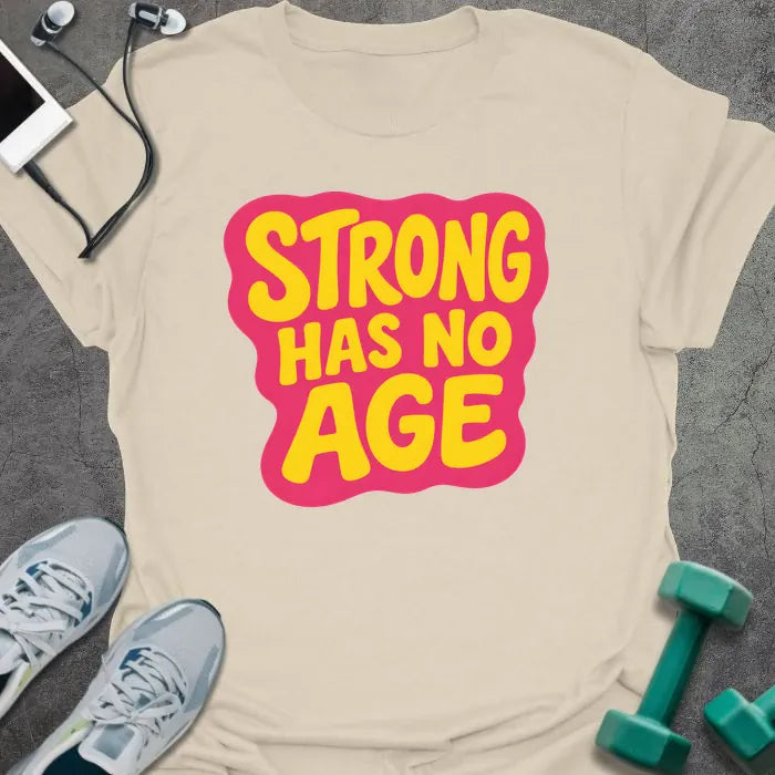 Natural t-shirt printed with "STRONG HAS NO AGE" in yellow and pink, with badge graphic